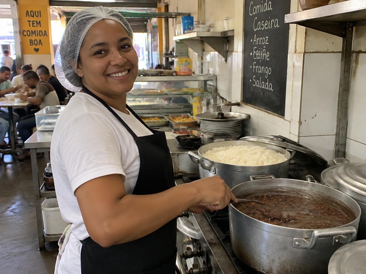 Cozinheira sorrindo enquanto prepara arroz e feijão em restaurante popular